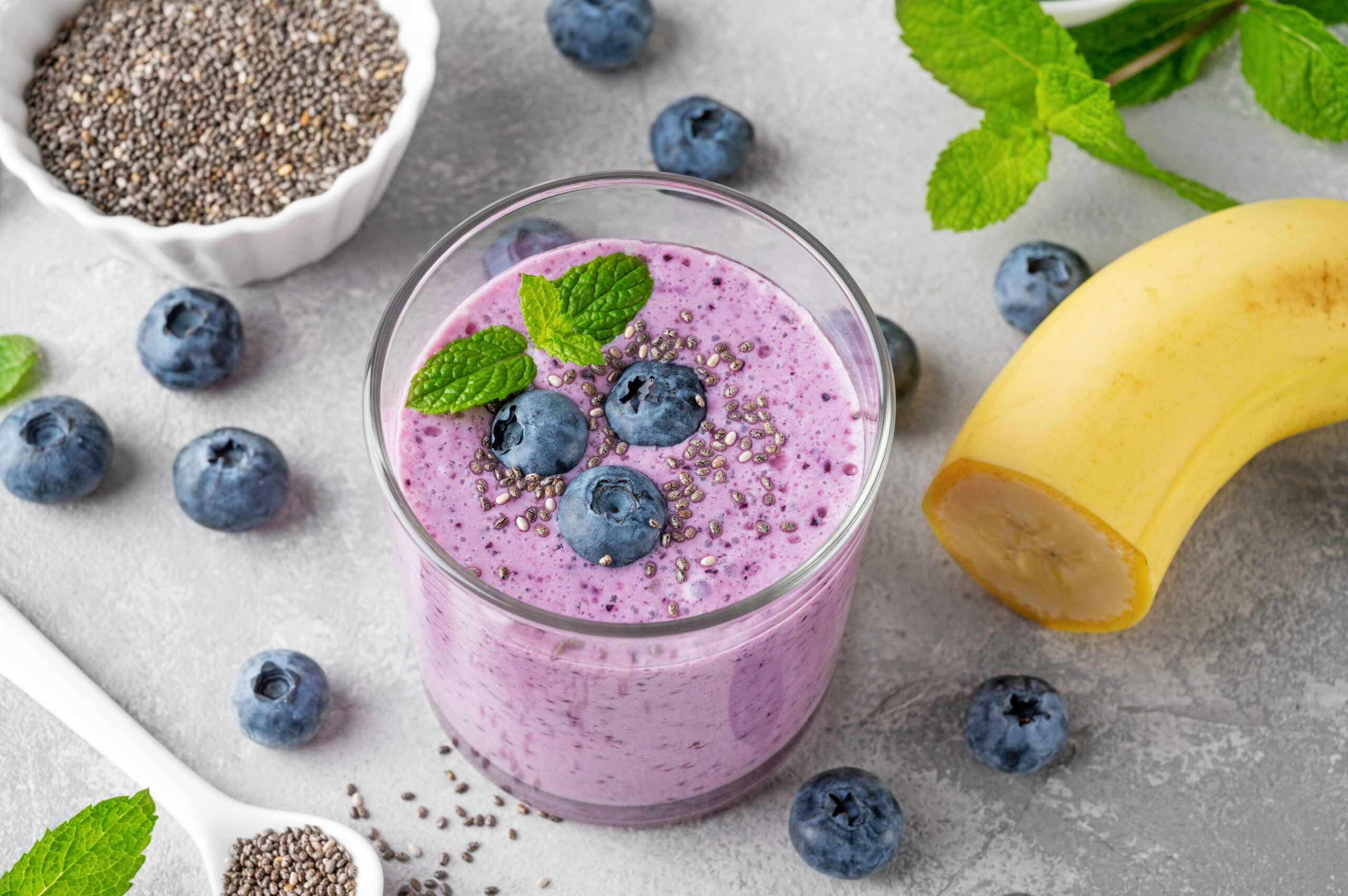 Smoothie with blueberries, banana, chia seeds and yogurt in a glass on a gray concrete background. Healthy food