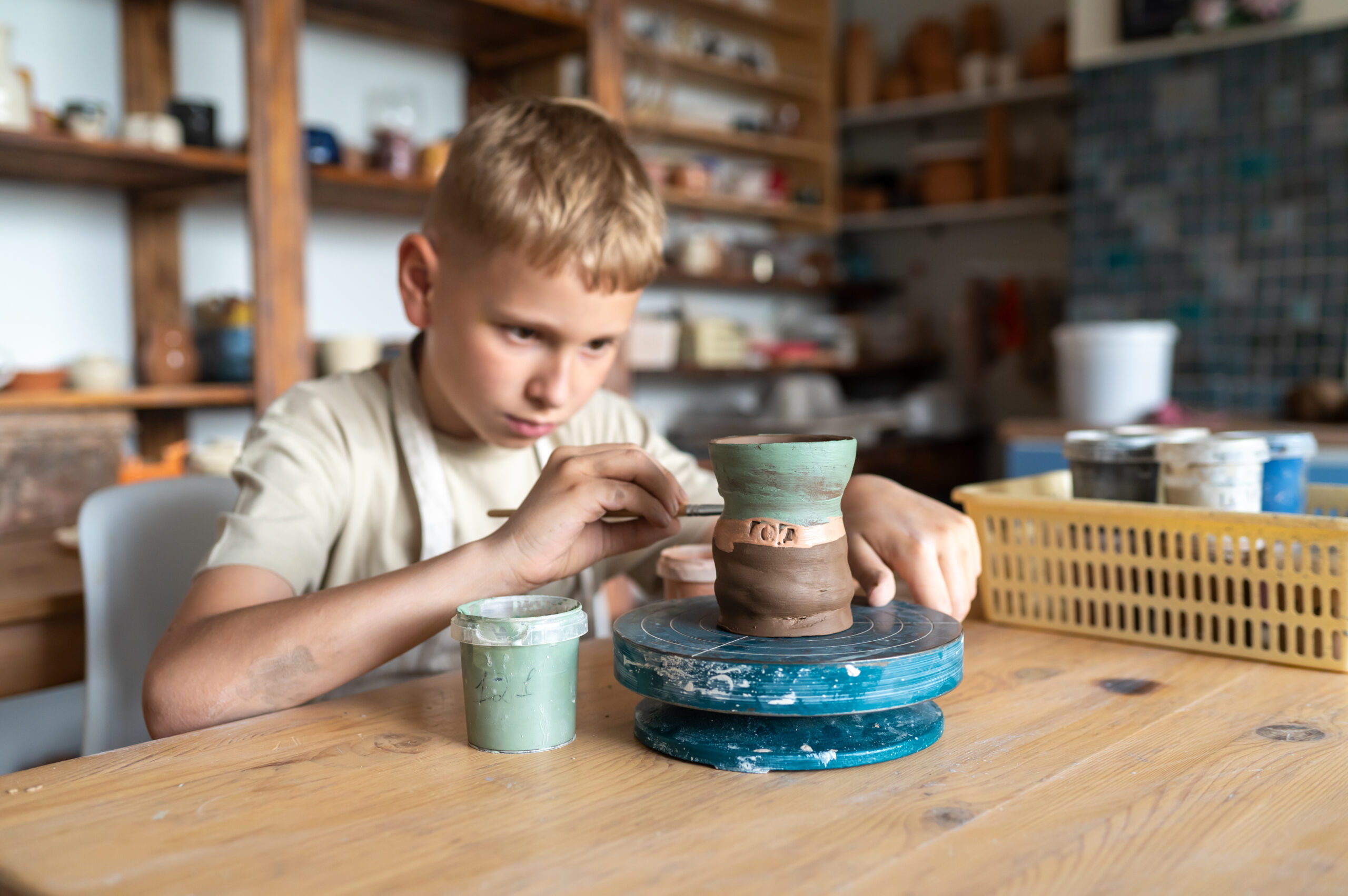 Blond boy carefully painting handmade clay cup, creative kids activity in cozy home pottery workshop